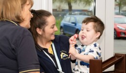 Illustration depicting two carers smiling whilst holding a child with special needs.