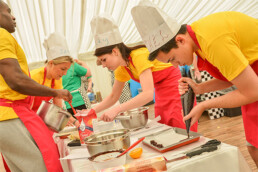 Illustration depicting a group of adults in aprons and chef hats gathered around a table baking.