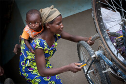 Illustration depicting a woman with a baby on her back whilst fixing a bike.