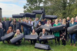 A picture showing a group of corporate clients holding up sleeping pods for homeless people to sleep in.